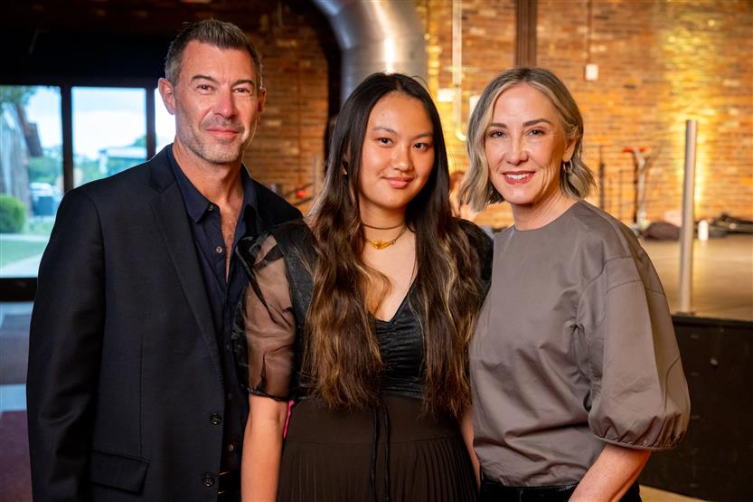 A man wearing black smiles with a woman wearing a black dress and a woman wearing a taupe top.